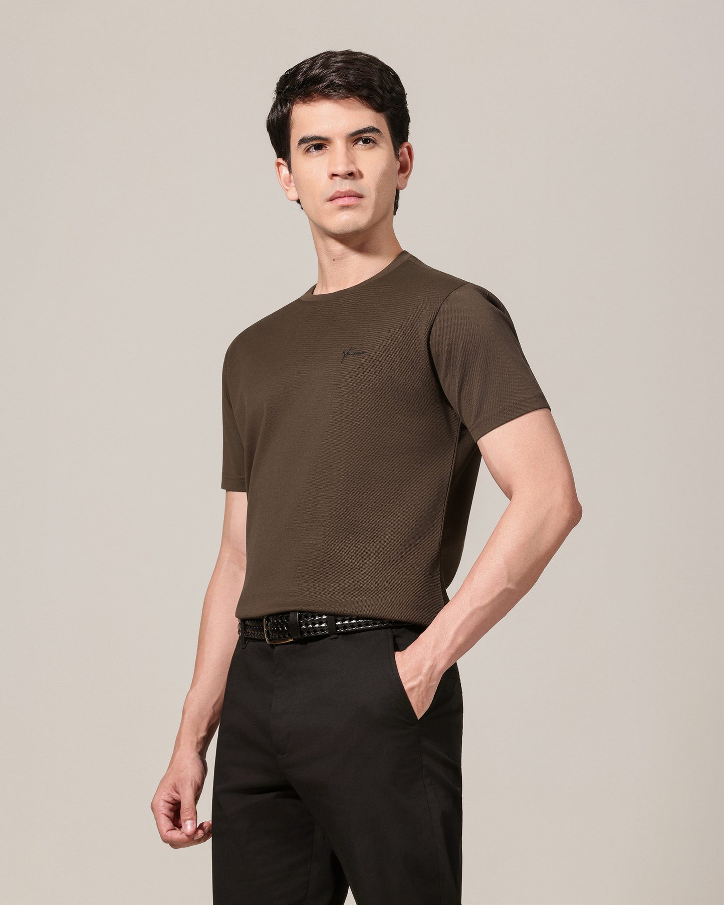 Man wearing a brown t-shirt and black pants against a beige background